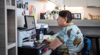 Vrouw werkt aan computer in ontmoetingshuis Aliado